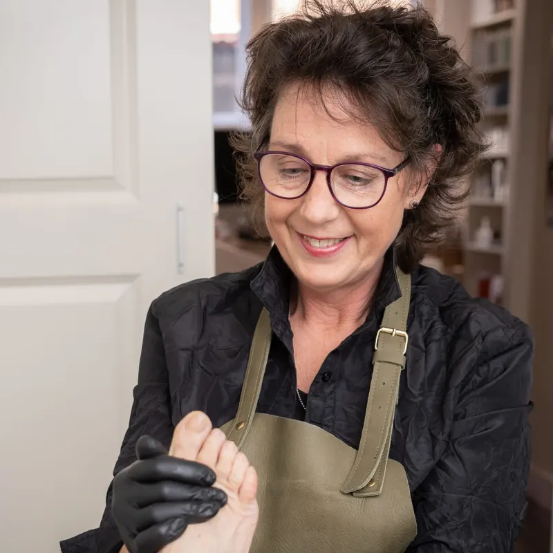 Sherryl Evertse in haar praktijk, met schort en handschoenen, houdt een voet vast